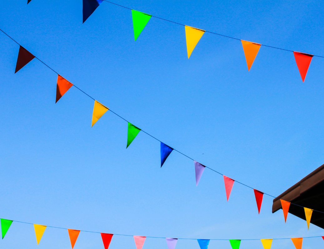Colorful fair pennant banners hanging against a clear blue sky, creating a festive atmosphere. Bannières colorées de kermesse suspendues dans le ciel bleu, créant une ambiance festive.